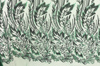 a close-up view of a fabric with a repeating pattern of green and black leaf-like designs. The pattern is intricate and detailed, with the leaves appearing to be made of sequins or other embellishments. The fabric has a textured appearance, suggesting it could be a type of clothing or textile.
