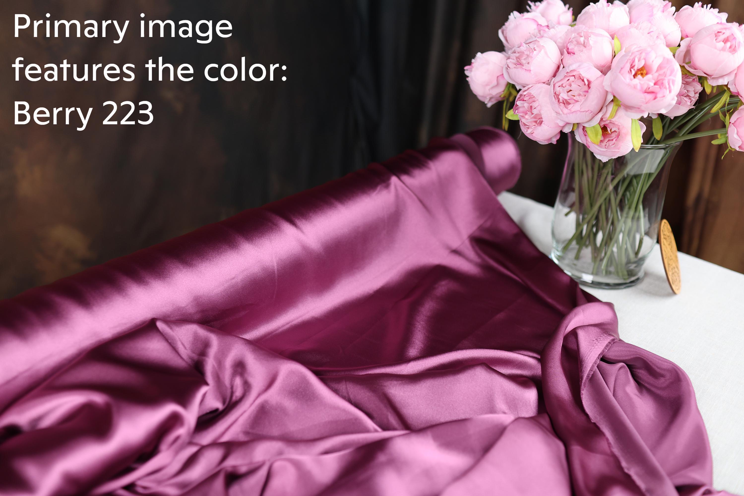 a close-up of a purple fabric with a vase of pink flowers on a table.