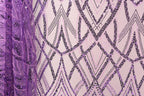 a close-up view of a fabric with a purple and black sequin pattern. The fabric appears to be a sheer material, with a repeating pattern of diagonal lines and shapes in shades of purple and black. The image does not contain any text or other discernible objects or actions.