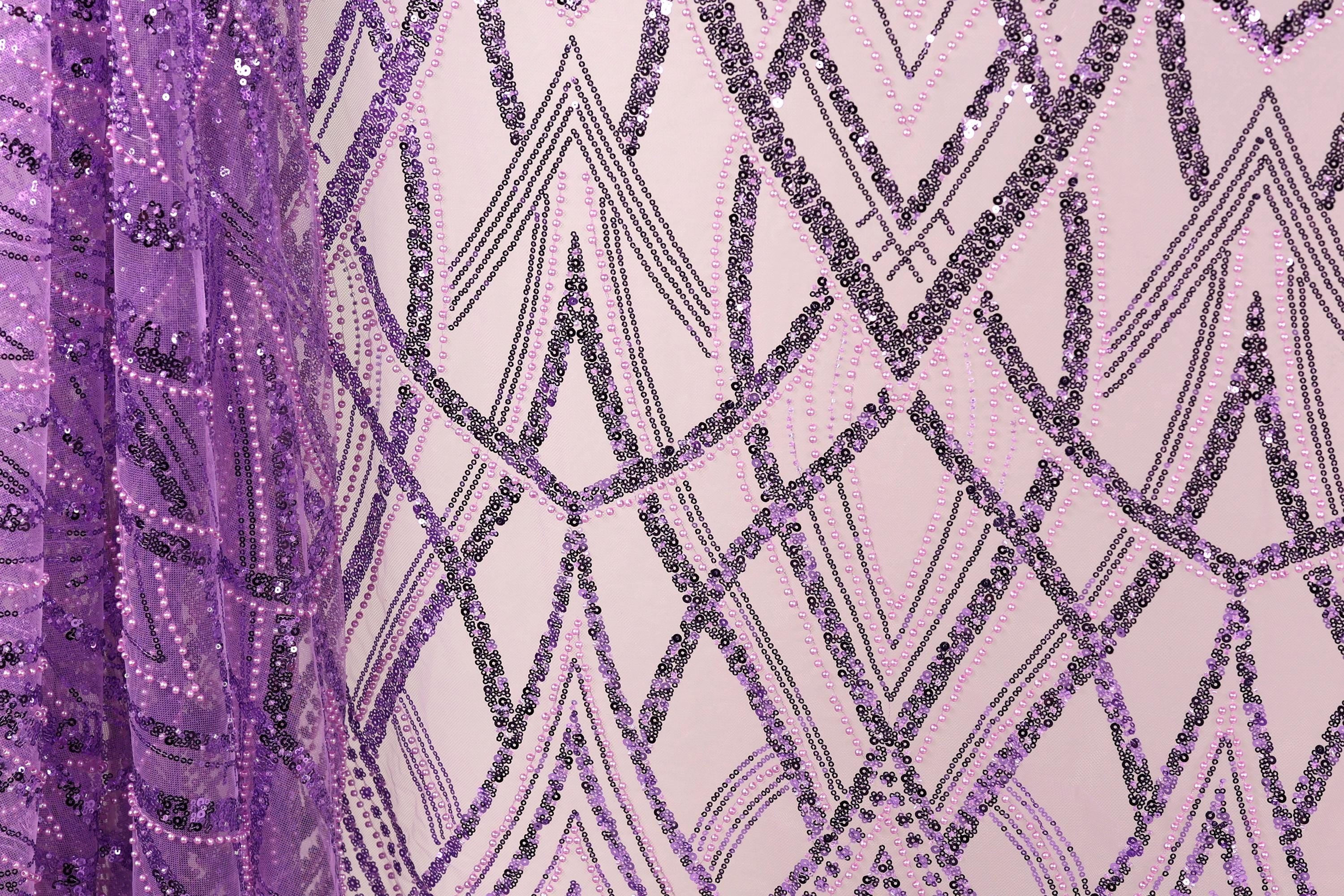 a close-up view of a fabric with a purple and black sequin pattern. The fabric appears to be a sheer material, with a repeating pattern of diagonal lines and shapes in shades of purple and black. The image does not contain any text or other discernible objects or actions.