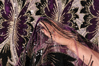 A close-up view of a hand holding a piece of fabric with a floral pattern in shades of purple and gold.
