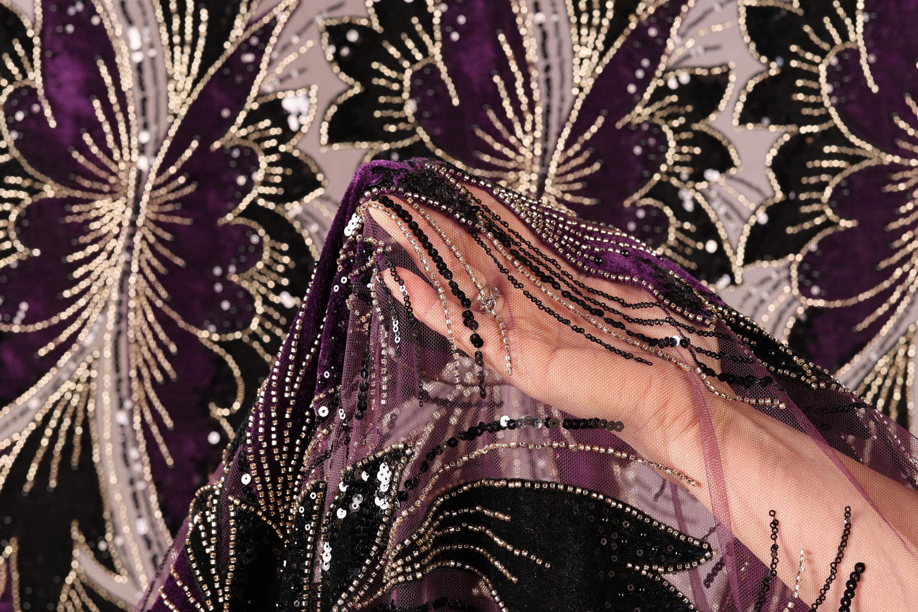 A close-up view of a hand holding a piece of fabric with a floral pattern in shades of purple and gold.