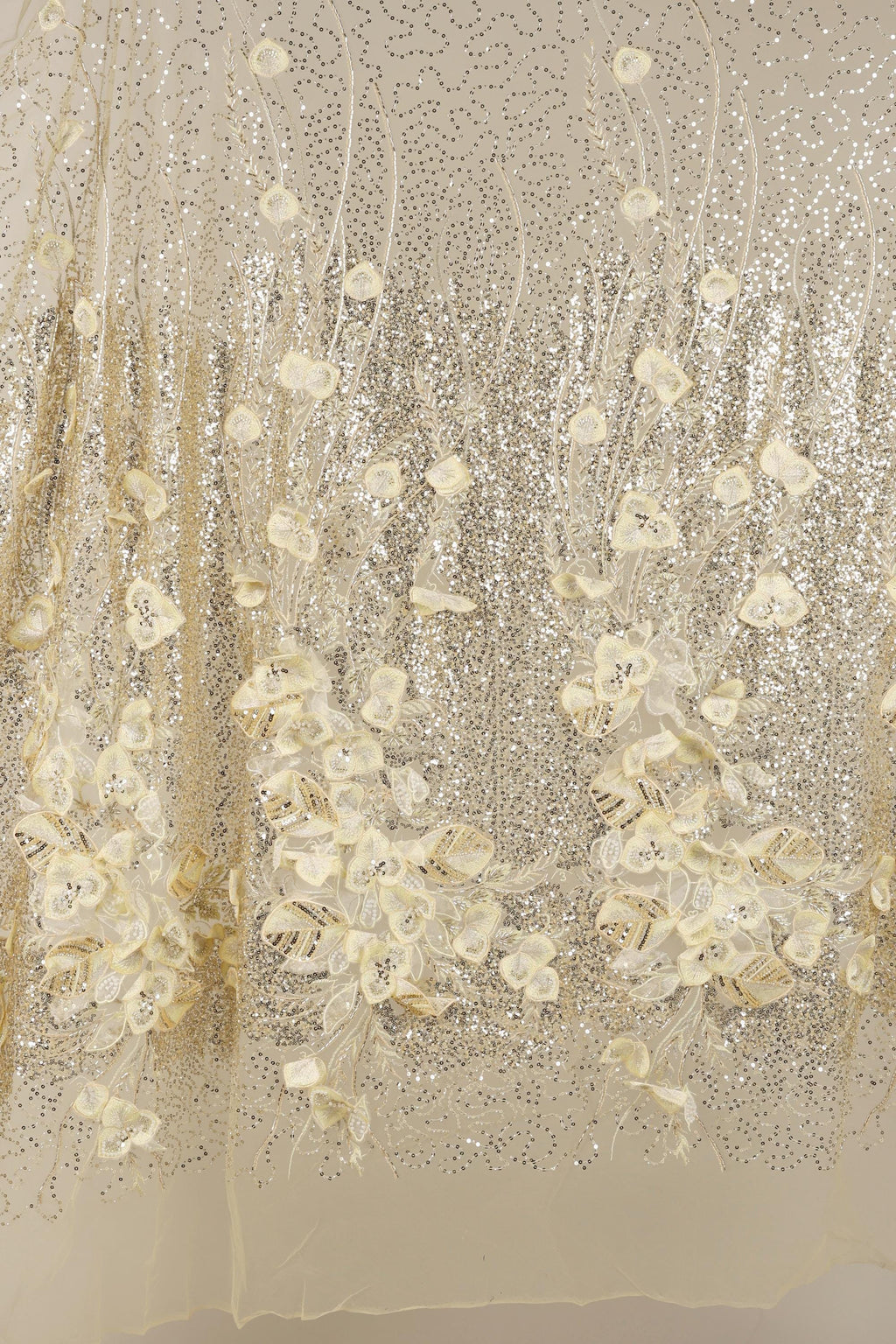 a close-up view of a delicate, shimmering fabric with a floral pattern. The fabric appears to be made of sequin material, giving it a sparkling and luxurious appearance. The floral design is intricate and detailed, with each flower and leaf meticulously crafted to create a visually appealing and elegant effect.