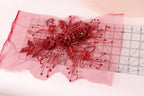 a close-up view of a red floral embellishment, possibly a piece of fabric or a decorative element, with a ruler placed on top of it.