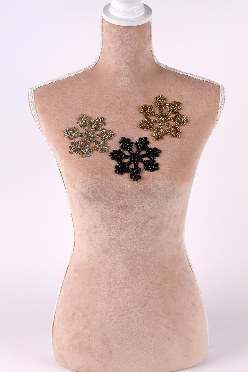 A mannequin with three different colored snowflake-shaped embellishments on its chest.