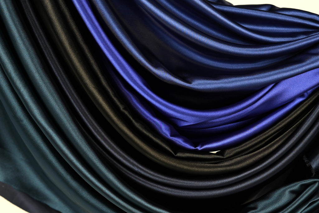 a close-up view of a pile of various colored satin fabric, including shades of blue, black, and green.