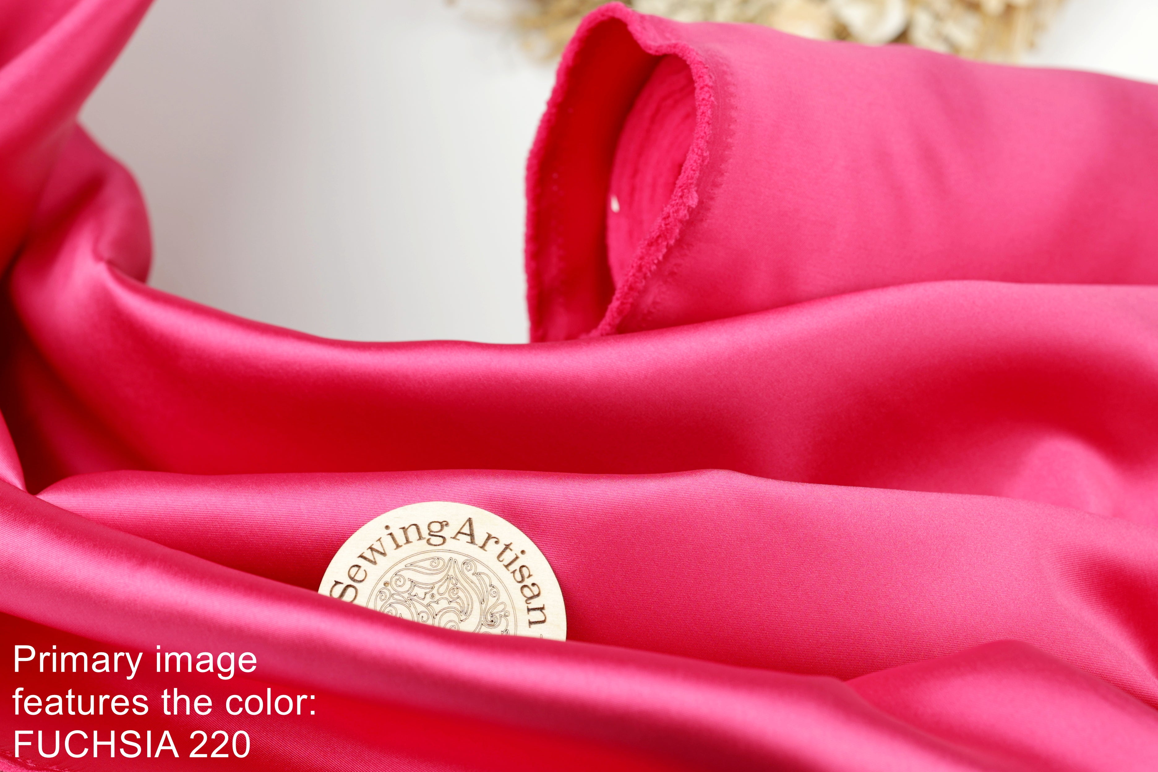 a close-up view of a vibrant pink satin fabric, with a small white label or emblem placed on it.