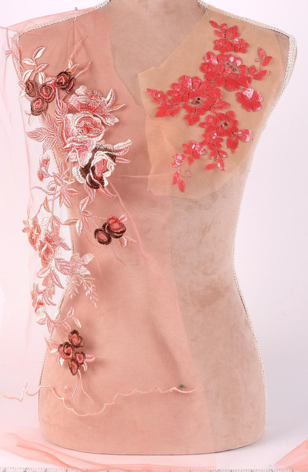 A mannequin with a pink fabric draped over it, featuring intricate floral embroidery in shades of red and pink.