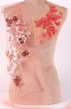 A mannequin with a pink fabric draped over it, featuring intricate floral embroidery in shades of red and pink.