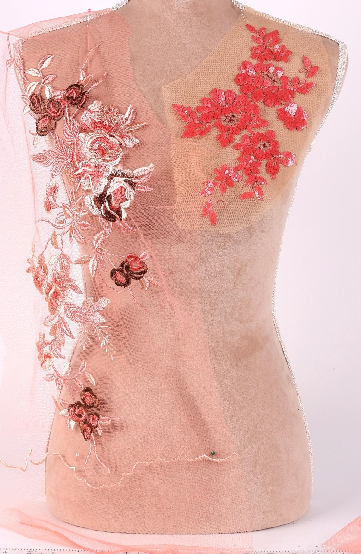 A mannequin with a pink fabric draped over it, featuring intricate floral embroidery in shades of red and pink.