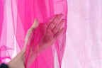 A hand is holding a pink, sparkly fabric against a pink background.