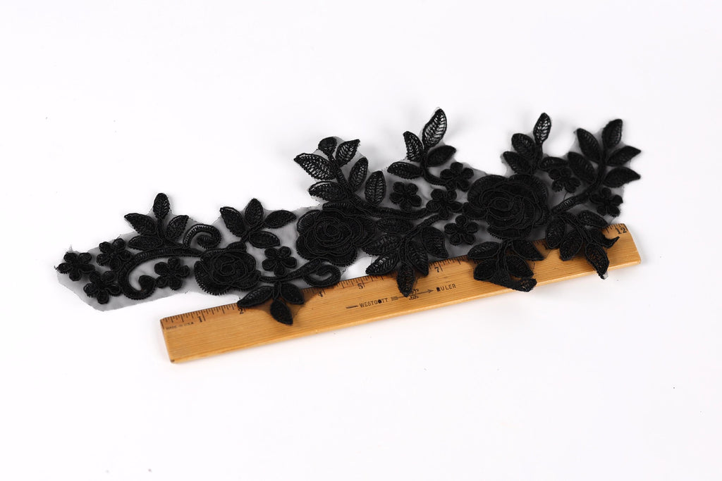 a black lace piece with intricate floral designs, placed on a wooden ruler for size reference.