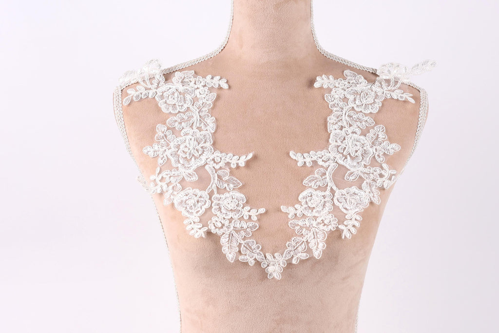 A mannequin wearing a white lace dress with intricate floral patterns.