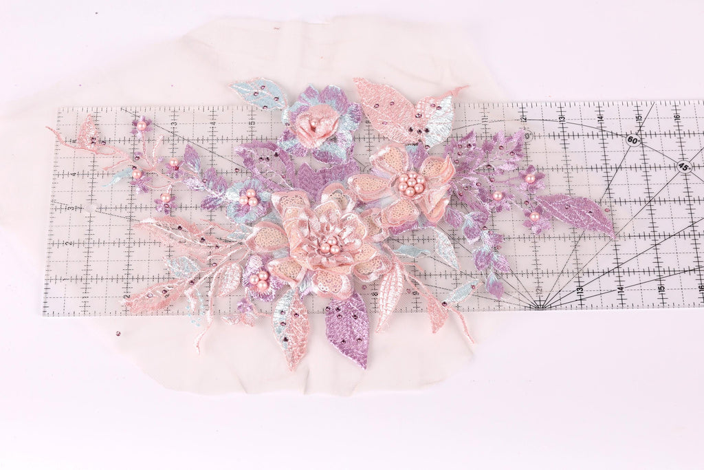a close-up view of a delicate floral embroidery with pink and purple flowers, leaves, and pearls. The embroidery appears to be crafted with precision and care, showcasing the intricate details of the design.