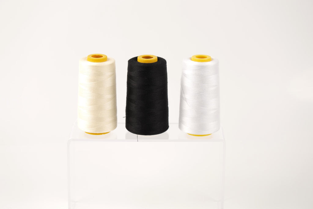 Three spools of thread in white, black, and white are displayed on a clear stand against a white background.