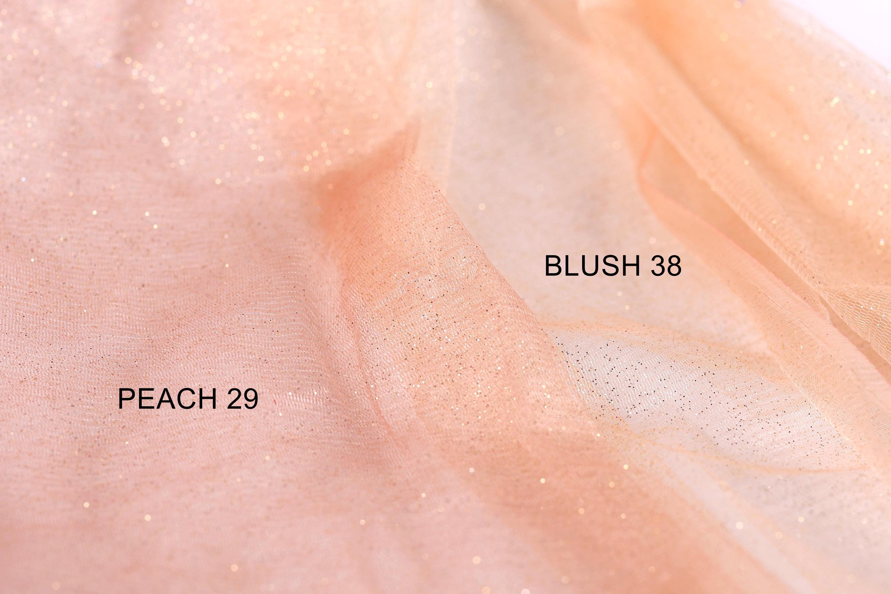 a close-up of a light peach-colored fabric with a glittery texture, with two labels indicating the fabric type and color.