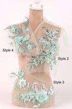A mannequin wearing a dress with various floral and leaf-like embroidered designs in shades of green and white.
