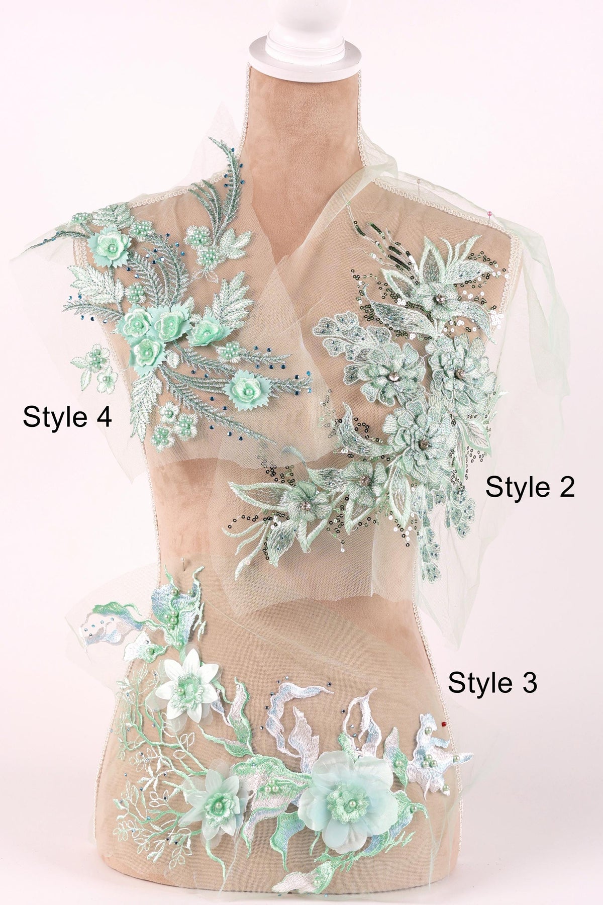A mannequin wearing a dress with various floral and leaf-like embroidered designs in shades of green and white.
