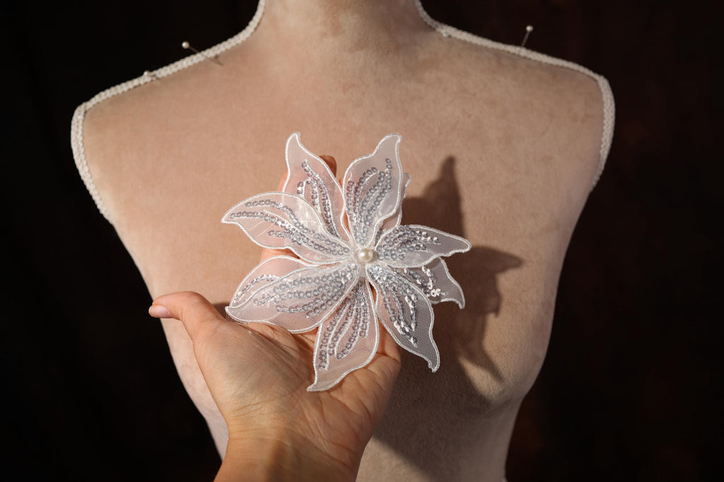 A hand holding a delicate white flower with sparkling embellishments against a dark background.