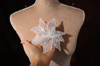 A hand holding a delicate white flower with sparkling embellishments against a dark background.