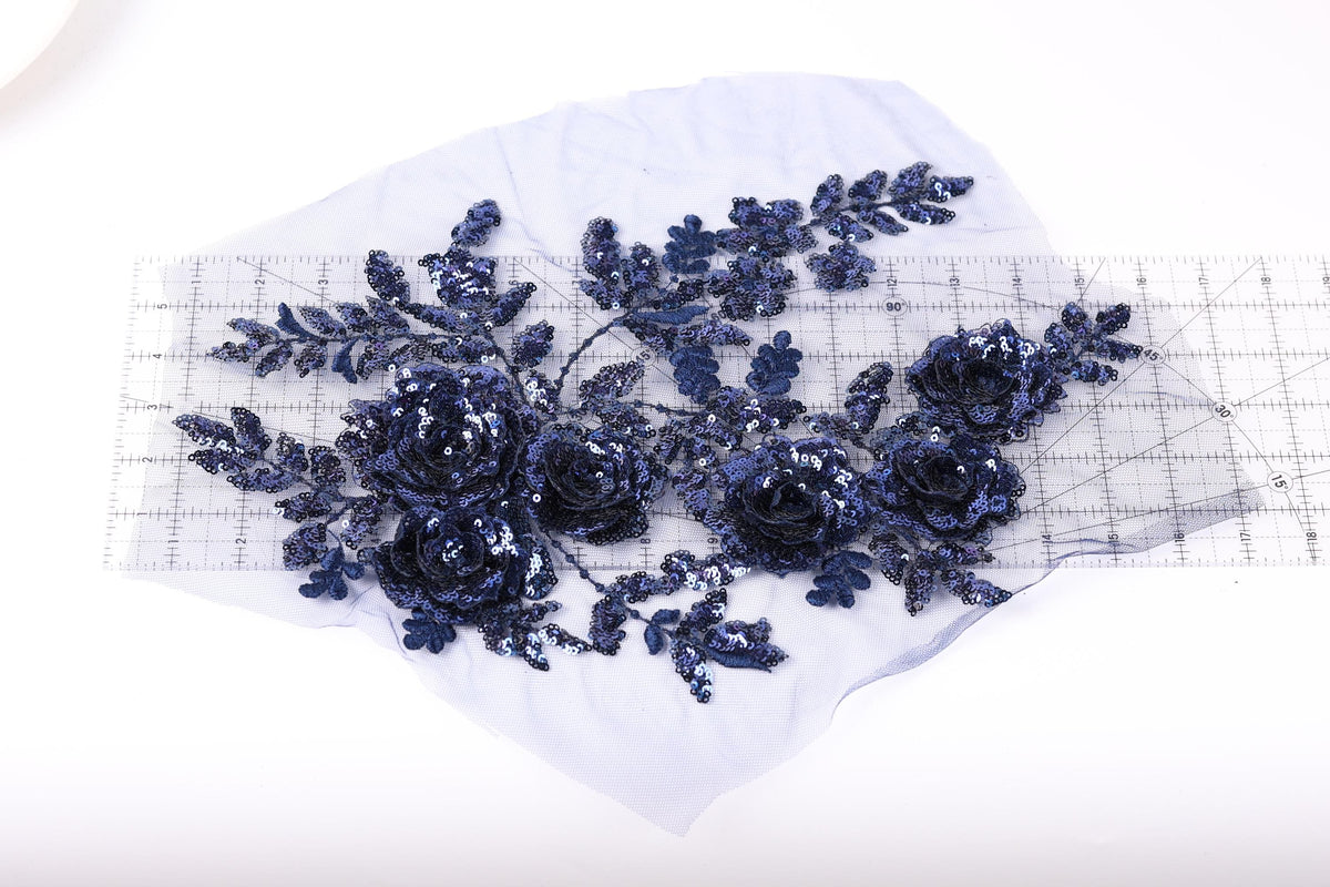 a close-up view of a piece of fabric with a floral design, including blue sequin flowers and leaves.