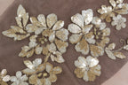 a close-up view of a fabric with intricate gold and white sequin designs, including flowers and leaves.