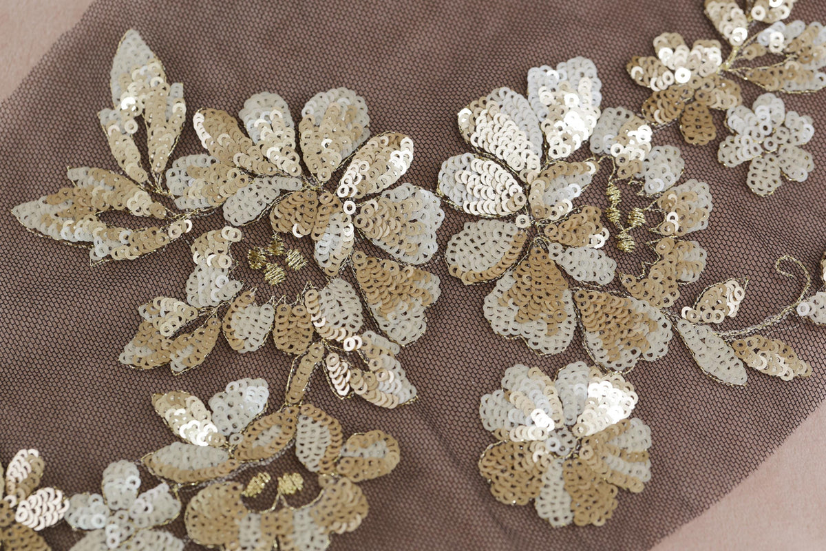 a close-up view of a fabric with intricate gold and white sequin designs, including flowers and leaves.