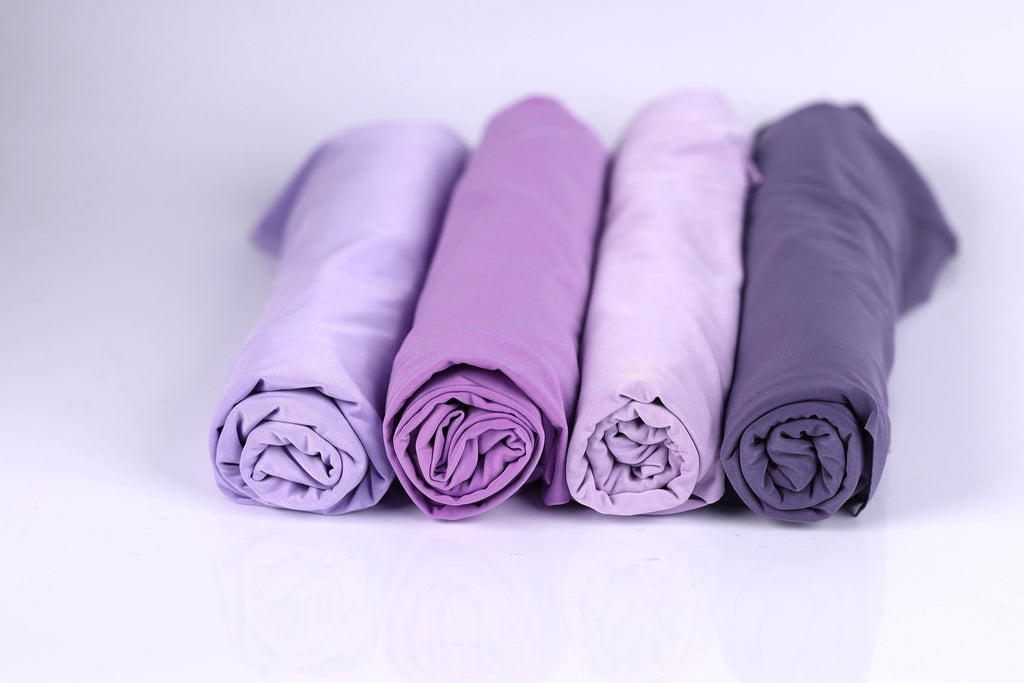 Four rolled-up fabric pieces in different shades of purple are arranged in a row on a white background.