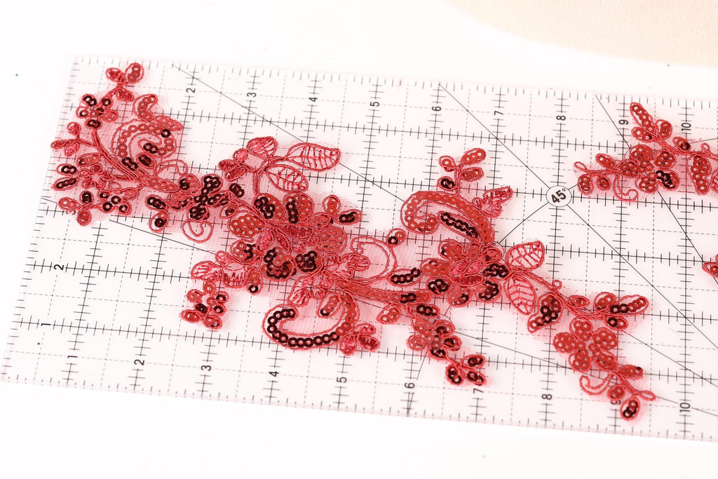 a close-up view of a red and black embroidered piece on a ruler, which appears to be a decorative element.