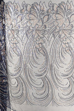 a close-up view of a fabric with a repeating pattern of silver and black sequin designs. The pattern consists of various shapes and swirls, creating a visually striking and intricate design. The fabric appears to be a light-colored material, possibly cotton or linen, with the silver and black sequins adding a touch of sparkle and elegance to the overall appearance.