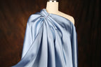 A mannequin wearing a blue satin one-shoulder dress with a draped, flowing silhouette.