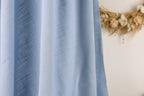 A close-up view of a blue fabric, possibly a curtain or textile, with a blurred floral wreath in the background.
