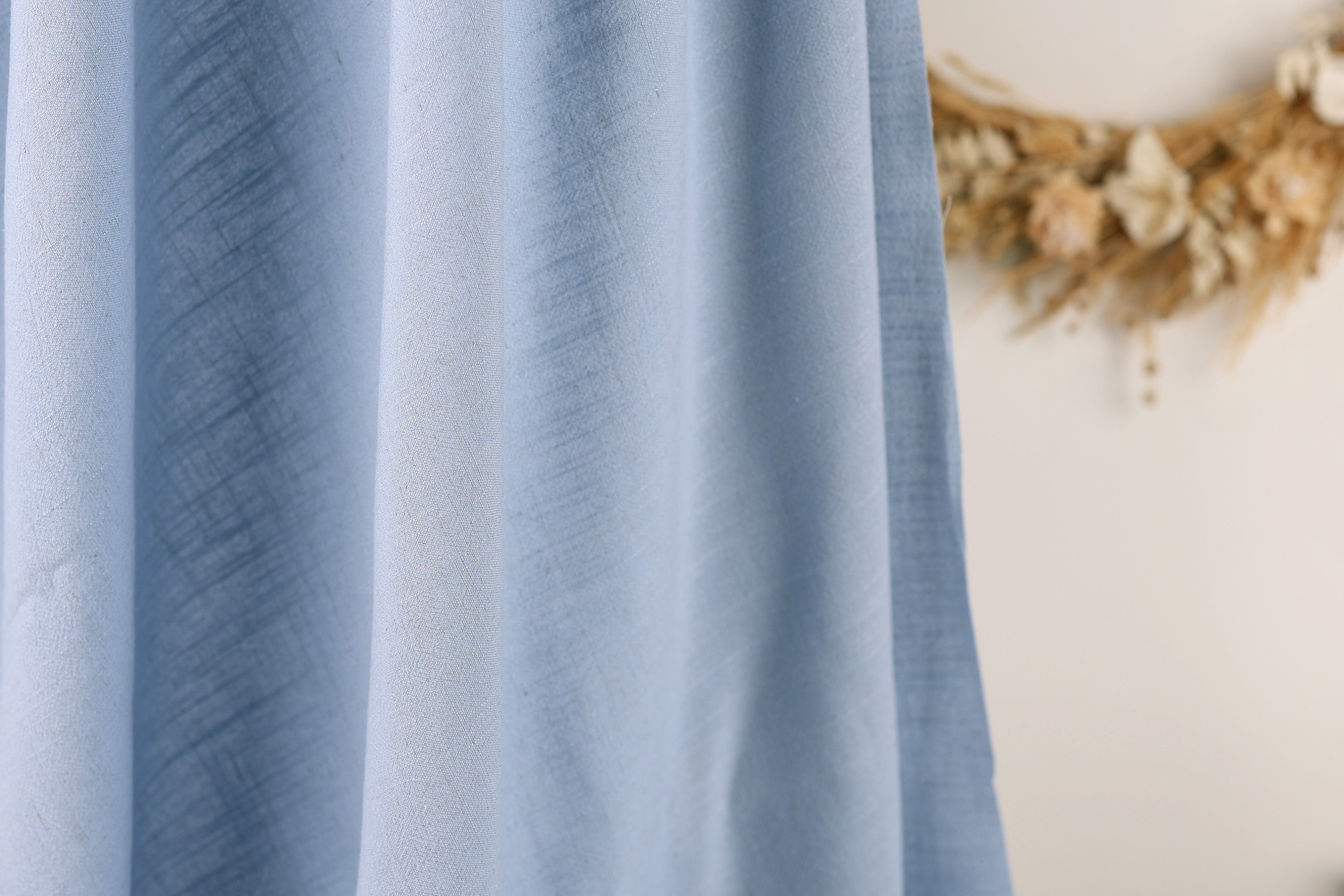 A close-up view of a blue fabric, possibly a curtain or textile, with a blurred floral wreath in the background.