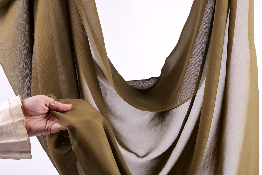 A hand is holding a piece of fabric, which appears to be a brown and white fabric, against a white background.