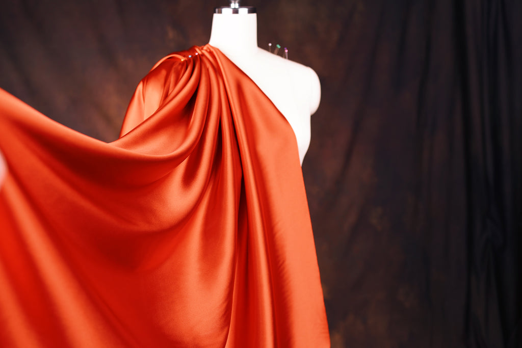 A mannequin wearing a flowing, orange satin cape against a dark background.