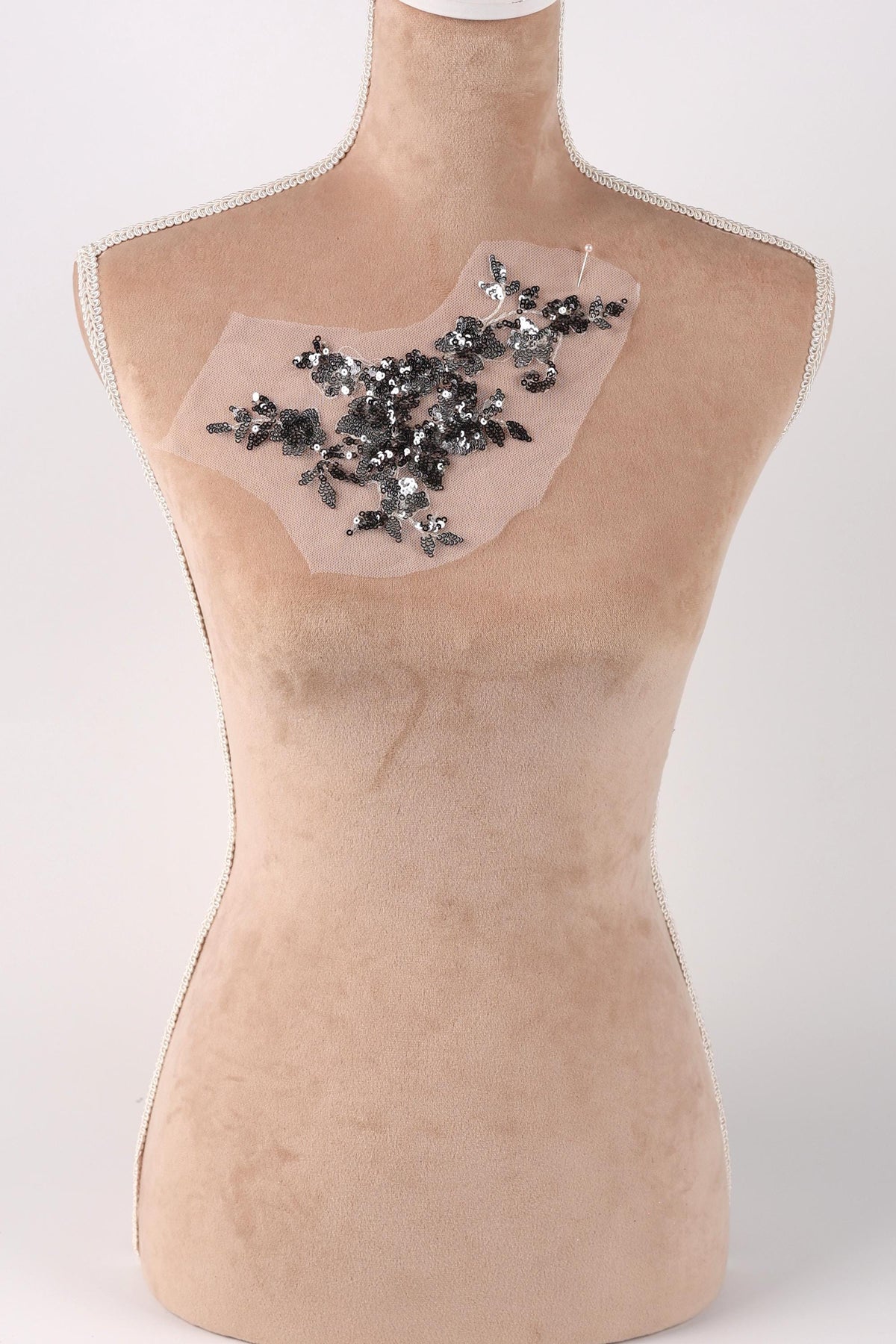 A mannequin with a beige body and a black and silver embellishment on its chest.