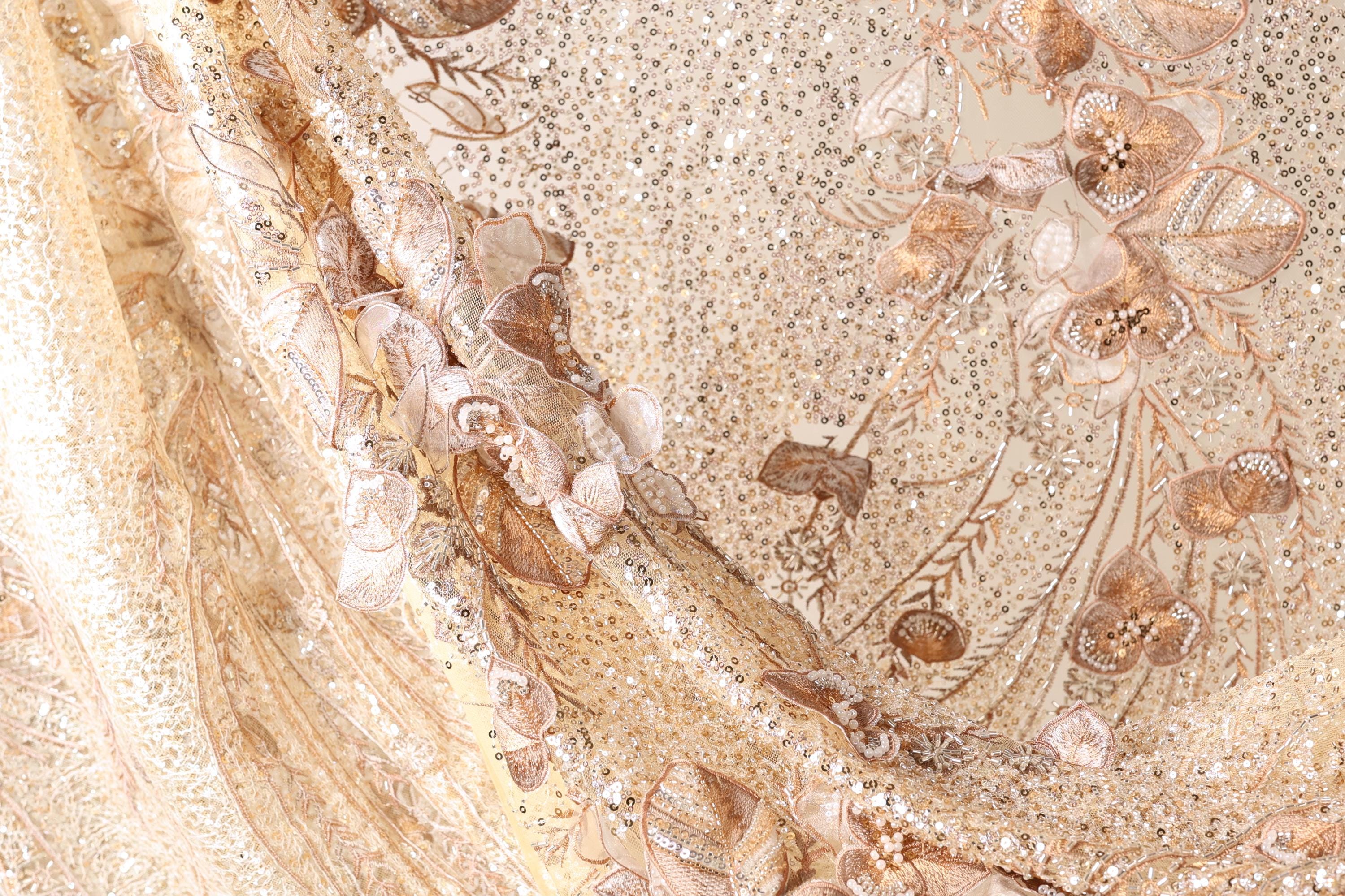 The image is a close-up of a fabric with a floral pattern, featuring gold and white colors.