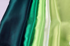 A close-up image of various colored satin fabric, including dark green, light green, and white, arranged in a vertical line.