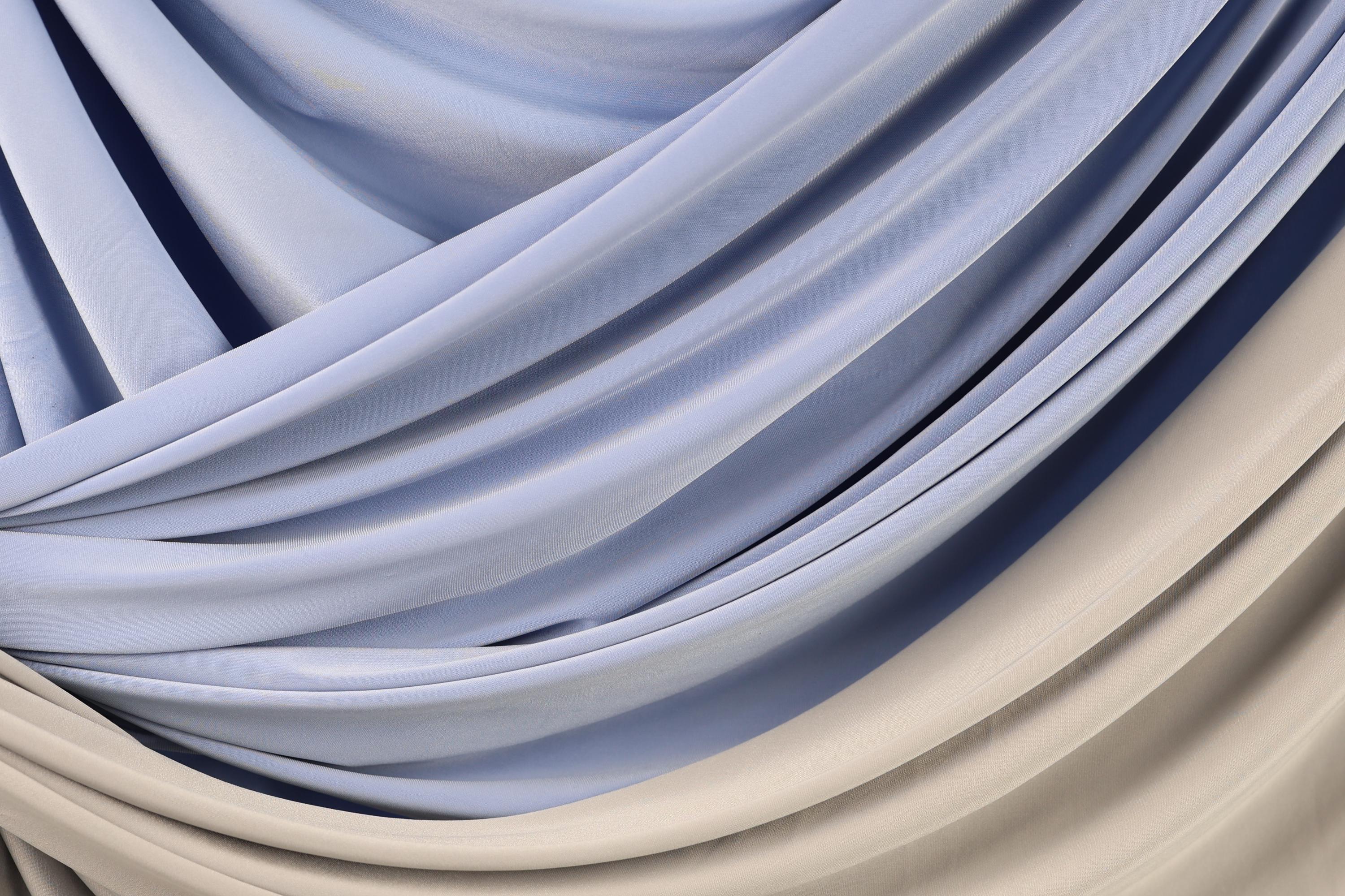 The image is a close-up of a fabric with a blue and beige color scheme, featuring a crumpled and draped appearance.