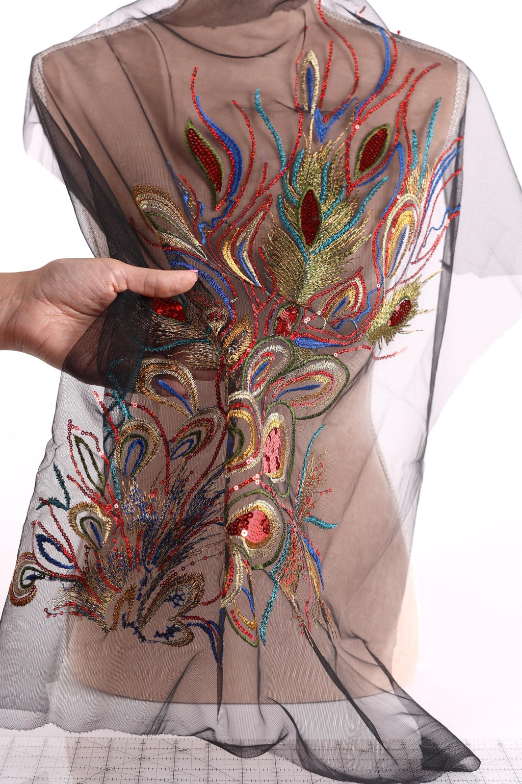 a hand holding a piece of sheer fabric with a colorful, intricate embroidered design on it.