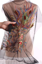 a hand holding a piece of sheer fabric with a colorful, intricate embroidered design on it.