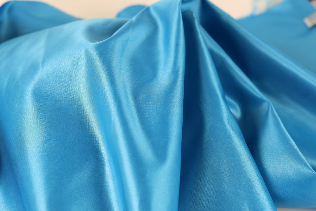 a close-up view of a blue satin fabric, with its smooth and shiny texture visible.