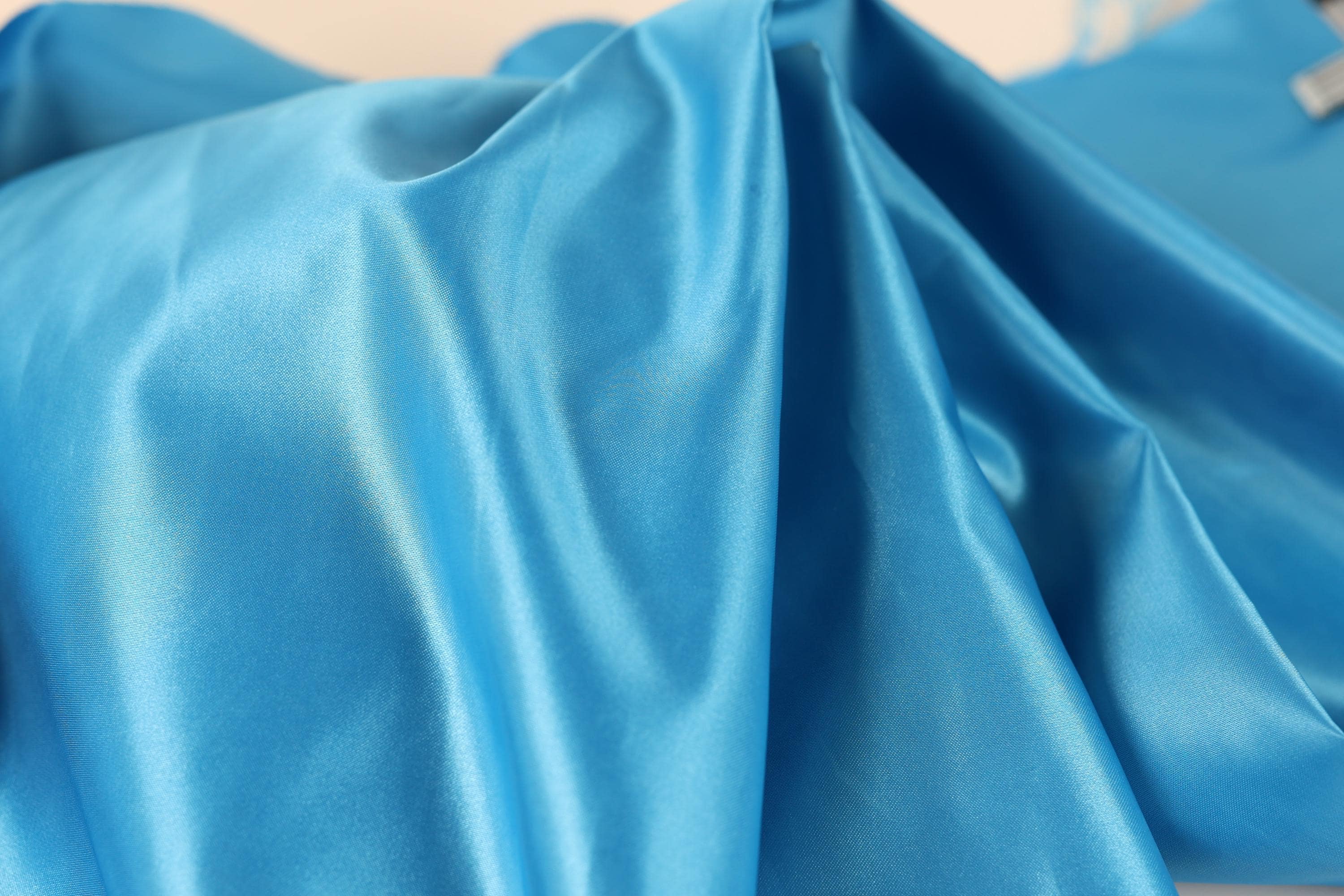 a close-up view of a blue satin fabric, with its smooth and shiny texture visible.