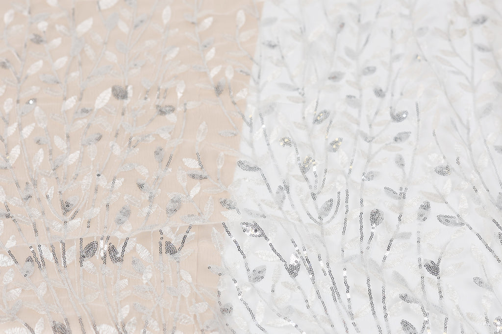 a close-up view of a fabric with a repeating pattern of silver and white sequin designs, resembling a tree or plant.