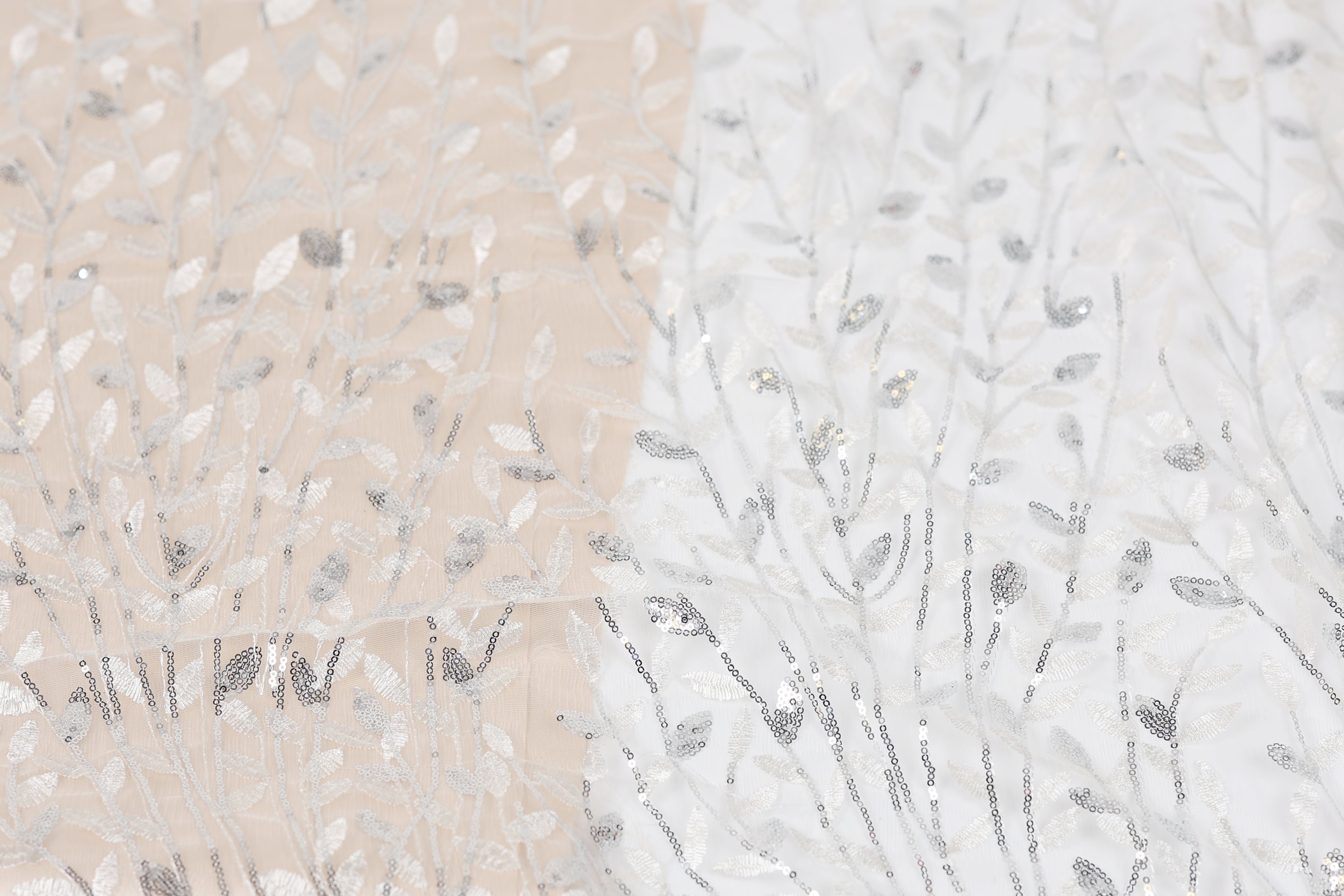 a close-up view of a fabric with a repeating pattern of silver and white sequin designs, resembling a tree or plant.