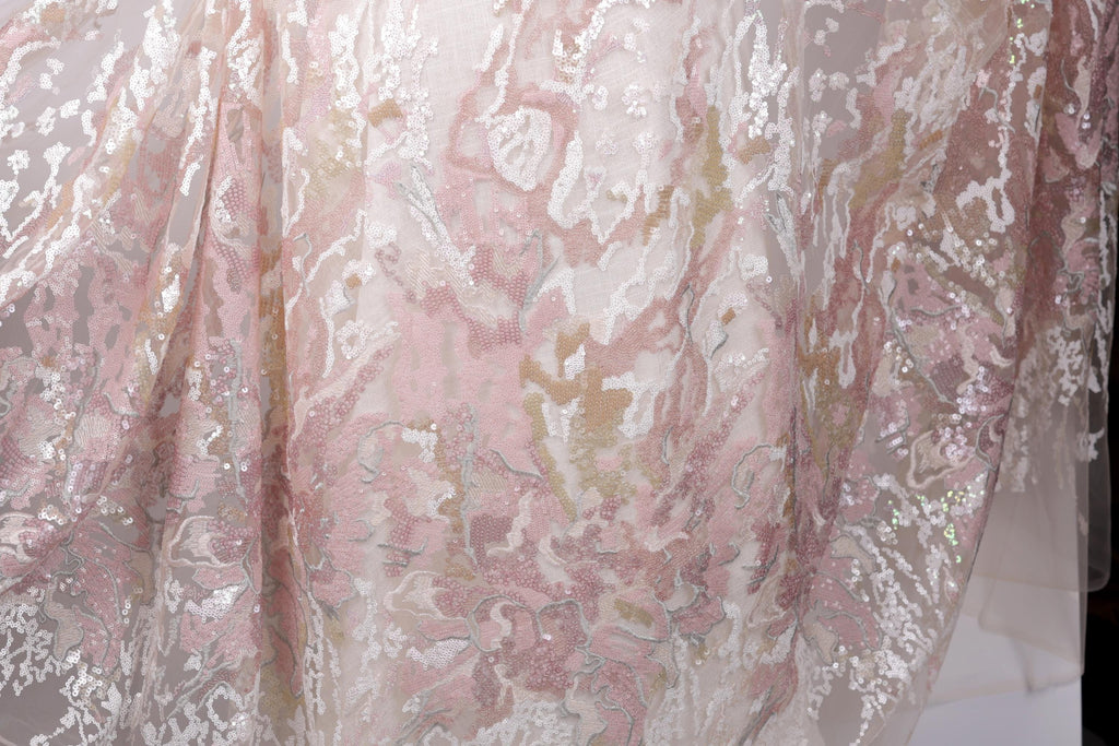 a close-up view of a delicate, lace-like fabric with a floral pattern in shades of pink and white. The fabric appears to be made of sheer material, giving it a delicate and airy appearance.