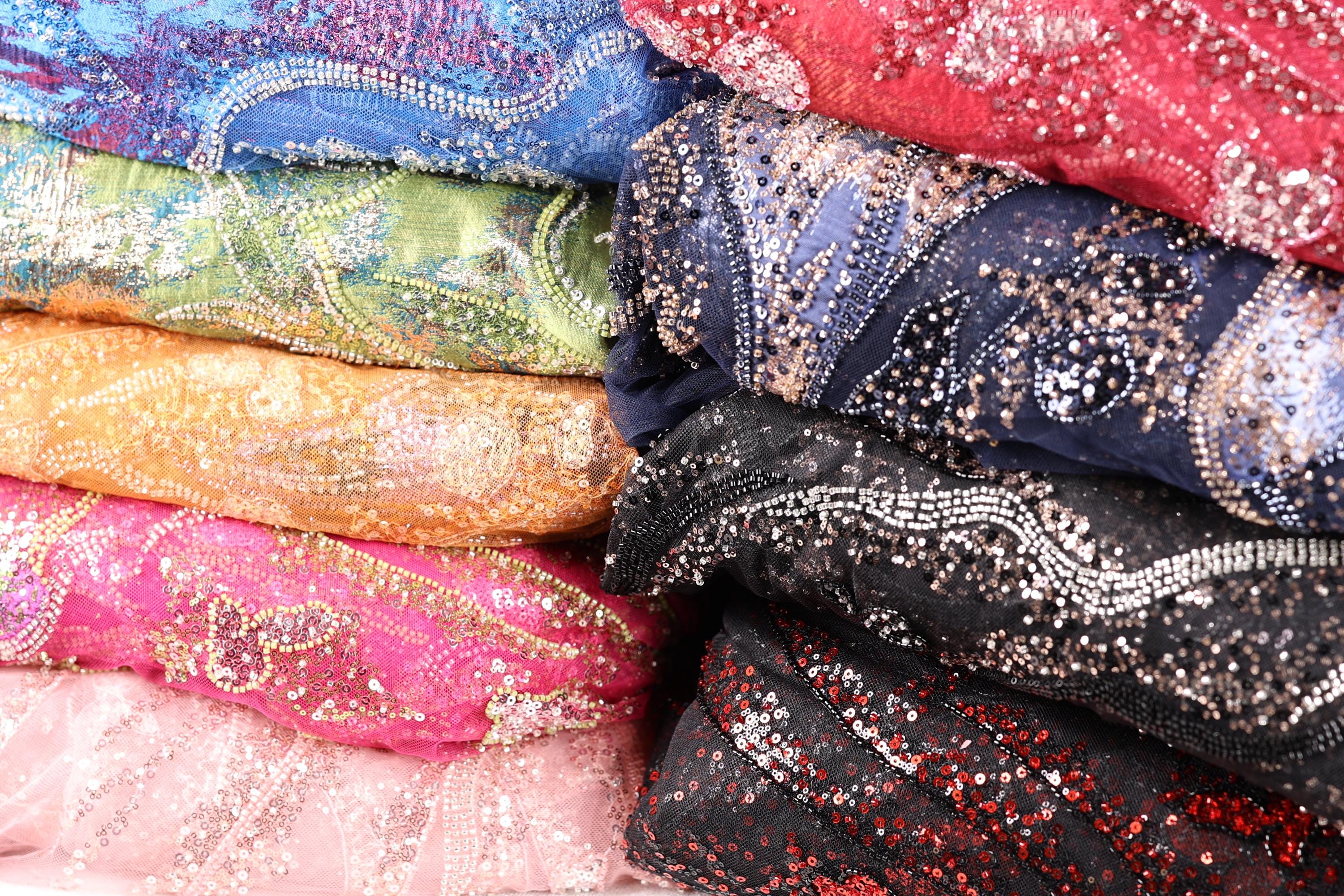 A close-up image of colorful, sequined fabric or material, with a variety of patterns and textures visible.