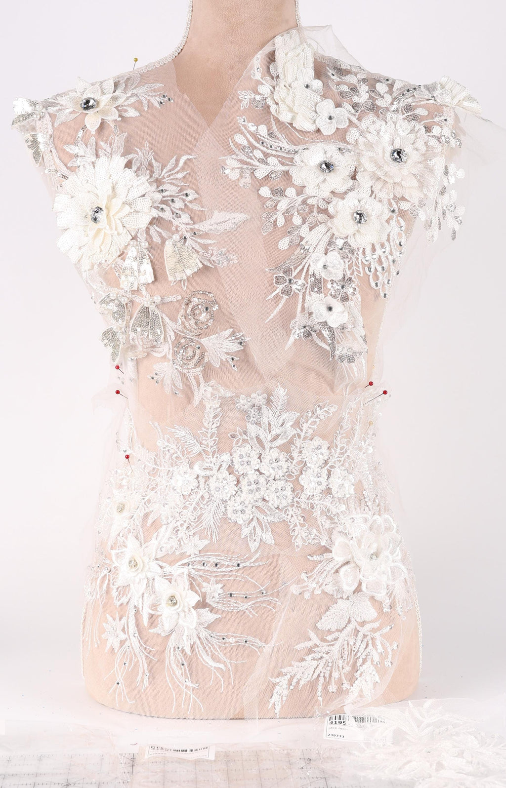 A mannequin wearing a white lace dress with intricate floral embroidery and beading details.