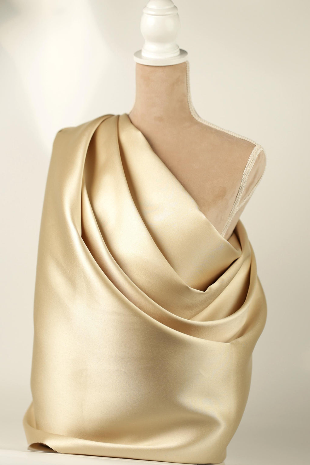 A mannequin is draped in a shiny, gold-colored fabric, which appears to be a draped garment.