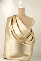 A mannequin is draped in a shiny, gold-colored fabric, which appears to be a draped garment.